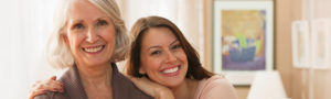 Mother and daughter smiling into the camera in a senior apartment living room